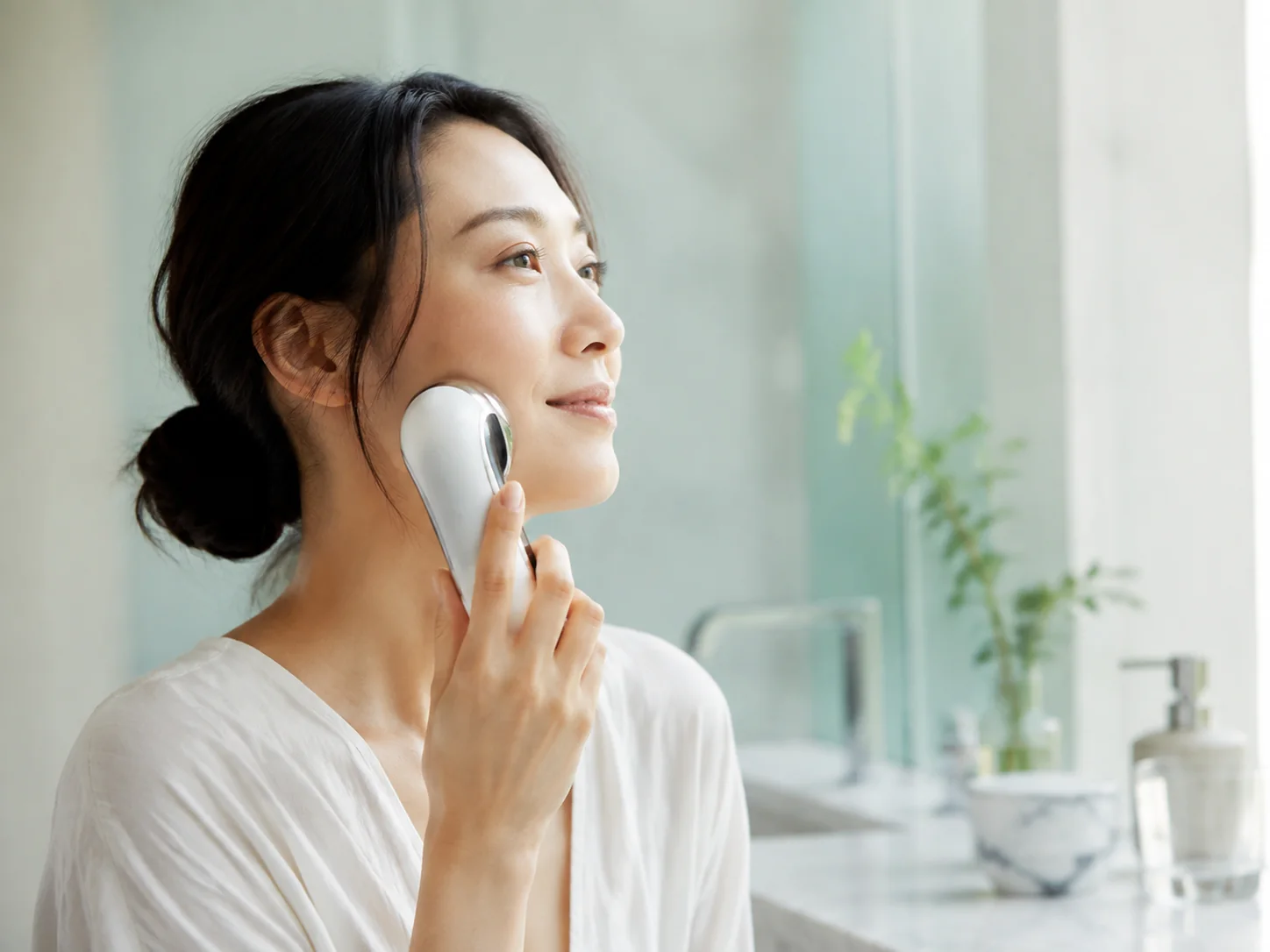 鏡の前で美顔器を頬に当てる女性